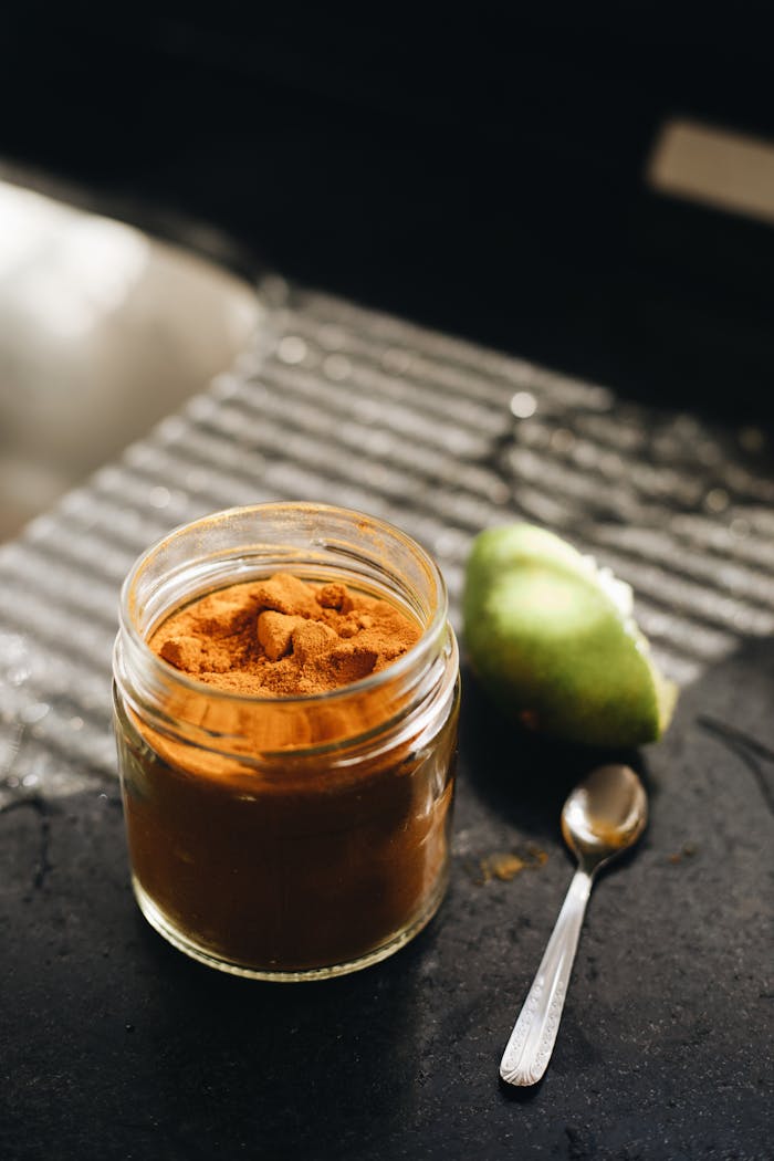 A close-up of a jar filled with turmeric powder next to a lime and spoon on a dark kitchen surface.