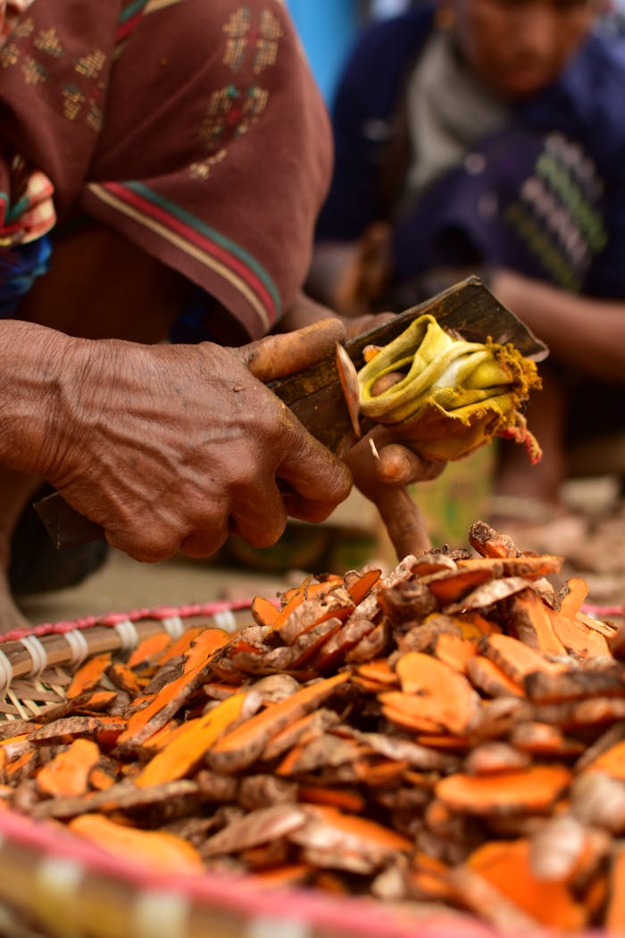 Close-up of an elderly hand cutting turmeric at a market stall in Shillong, India.