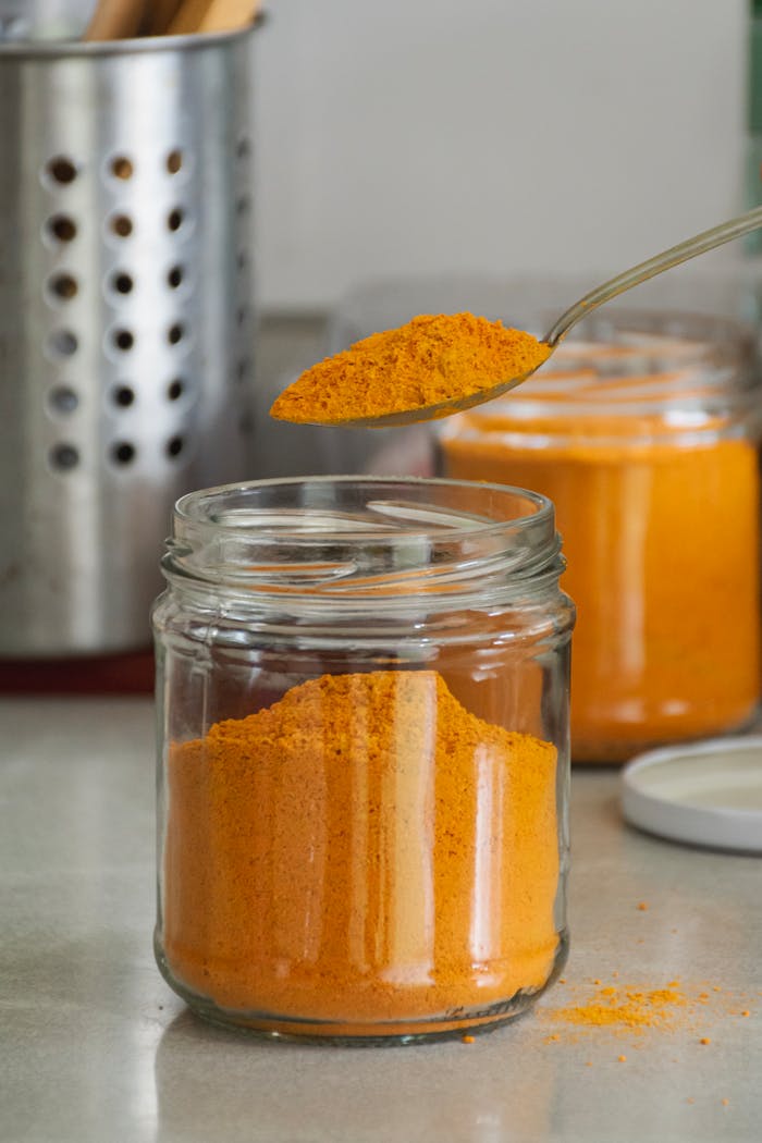 Close-up of bright turmeric powder in glass jars with spoon, enhancing culinary and health experiences.