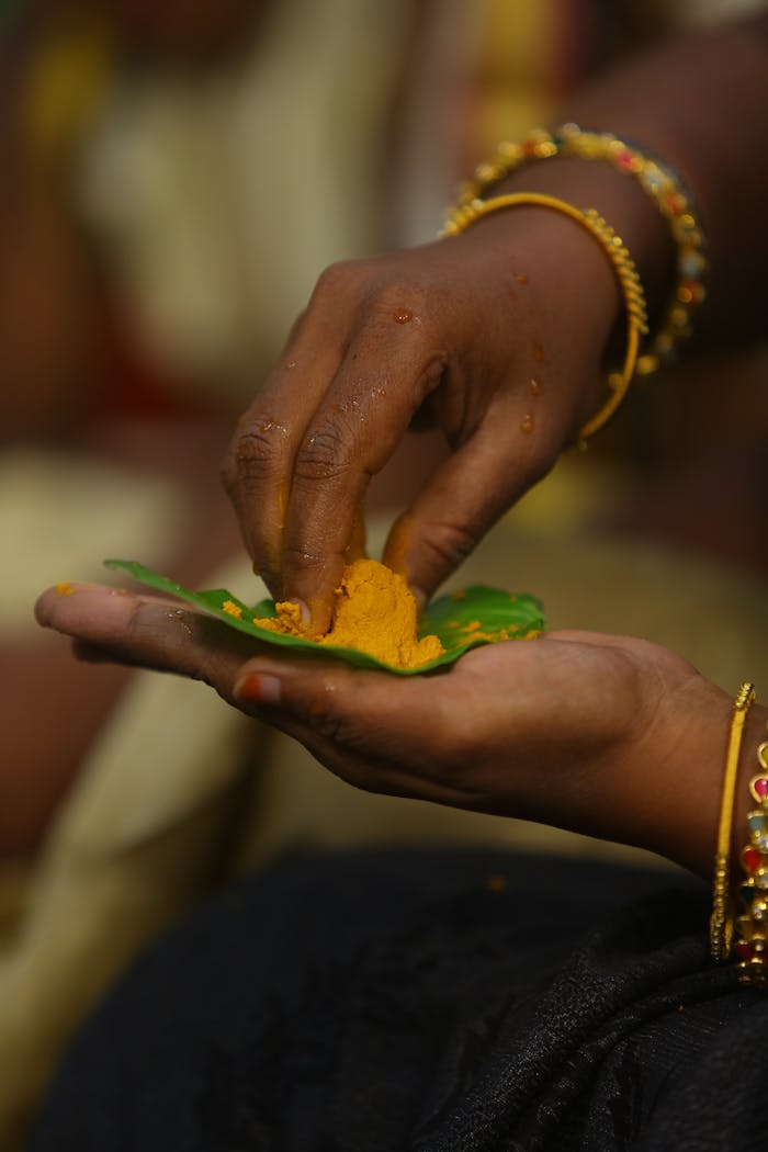 Close-up of hands applying turmeric on a betel leaf during a traditional ceremony.