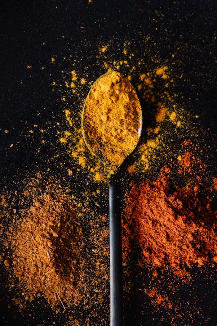 Top view of heap of powdered paprika and mix of peppers with bright curcuma in center on tablespoon on black background