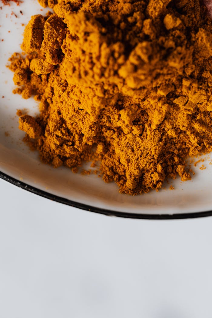 Top view of small heaps of powdered curcuma spice in metal bowl on white desktop